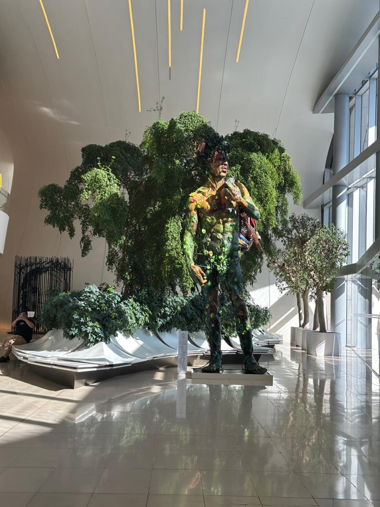 Large colorful human sculpture surrounded by greenery inside Heydar Aliyev Center in Baku